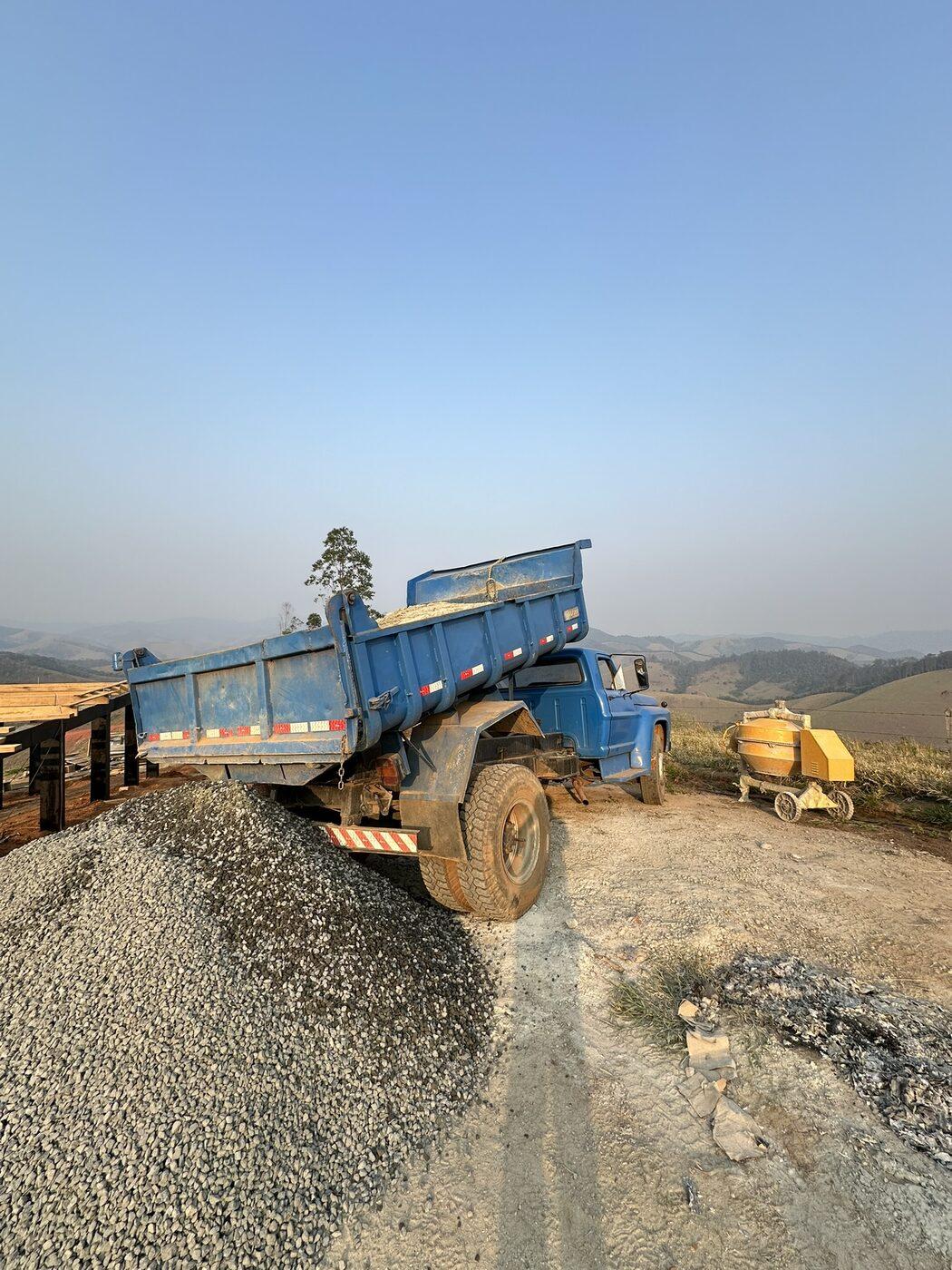 Caminhão azul basculando pedra em entrega
